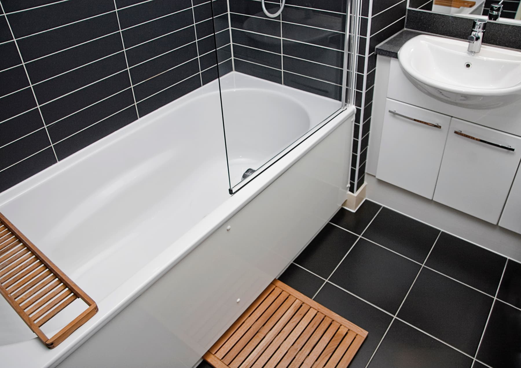 Bathroom with a tub, glass screen and dark tile