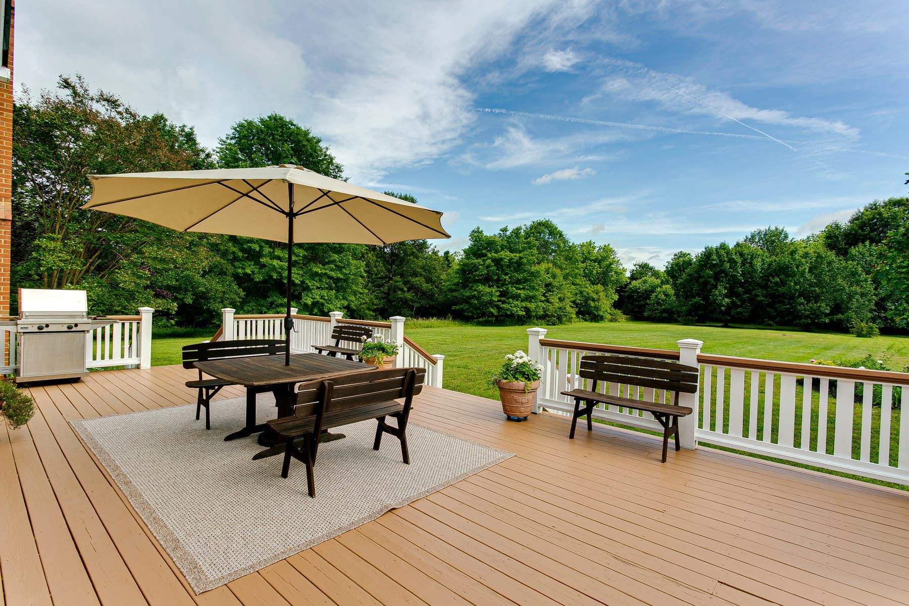 Deck with white railing, dining table and umbrella overlooking a lawn