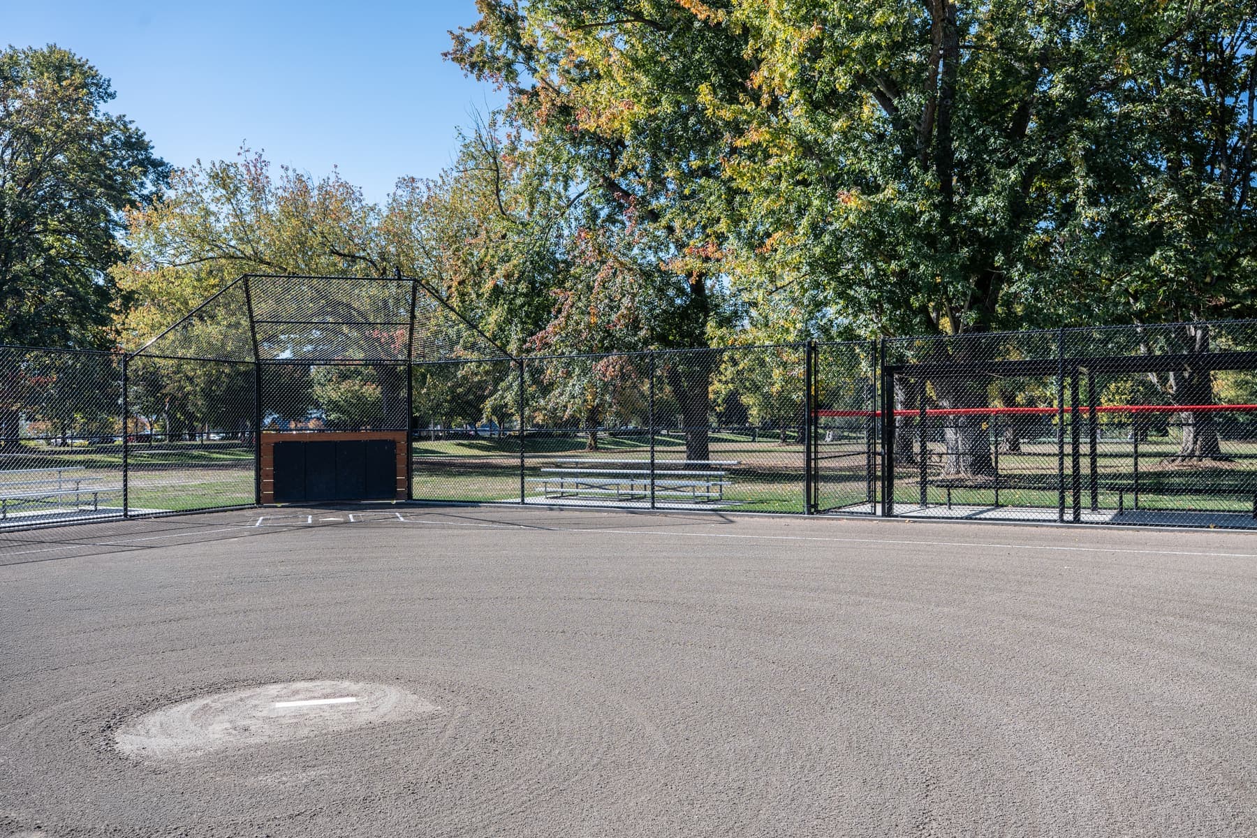 Ballfield backstop and dugout fencing in black chain-link, seen from the infield