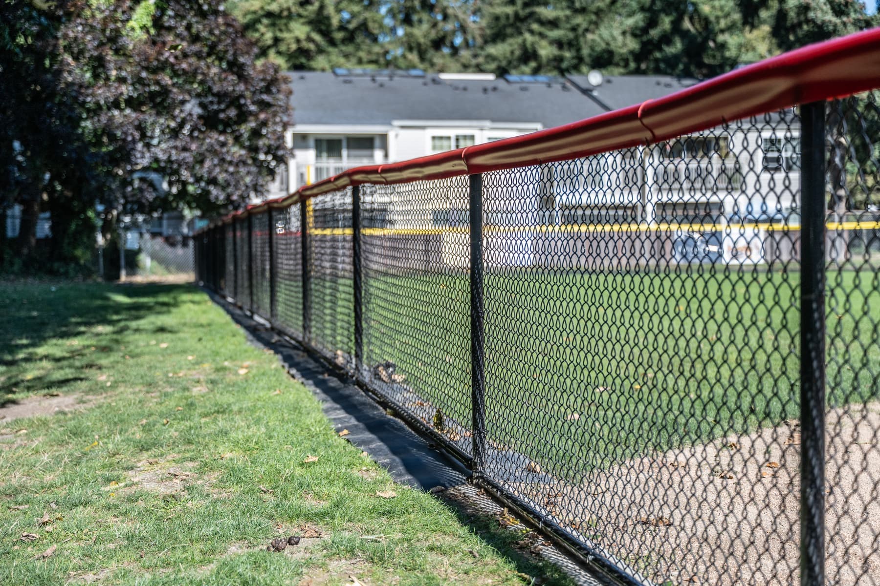 Black chain-link fence with a red top cap running along a ballfield