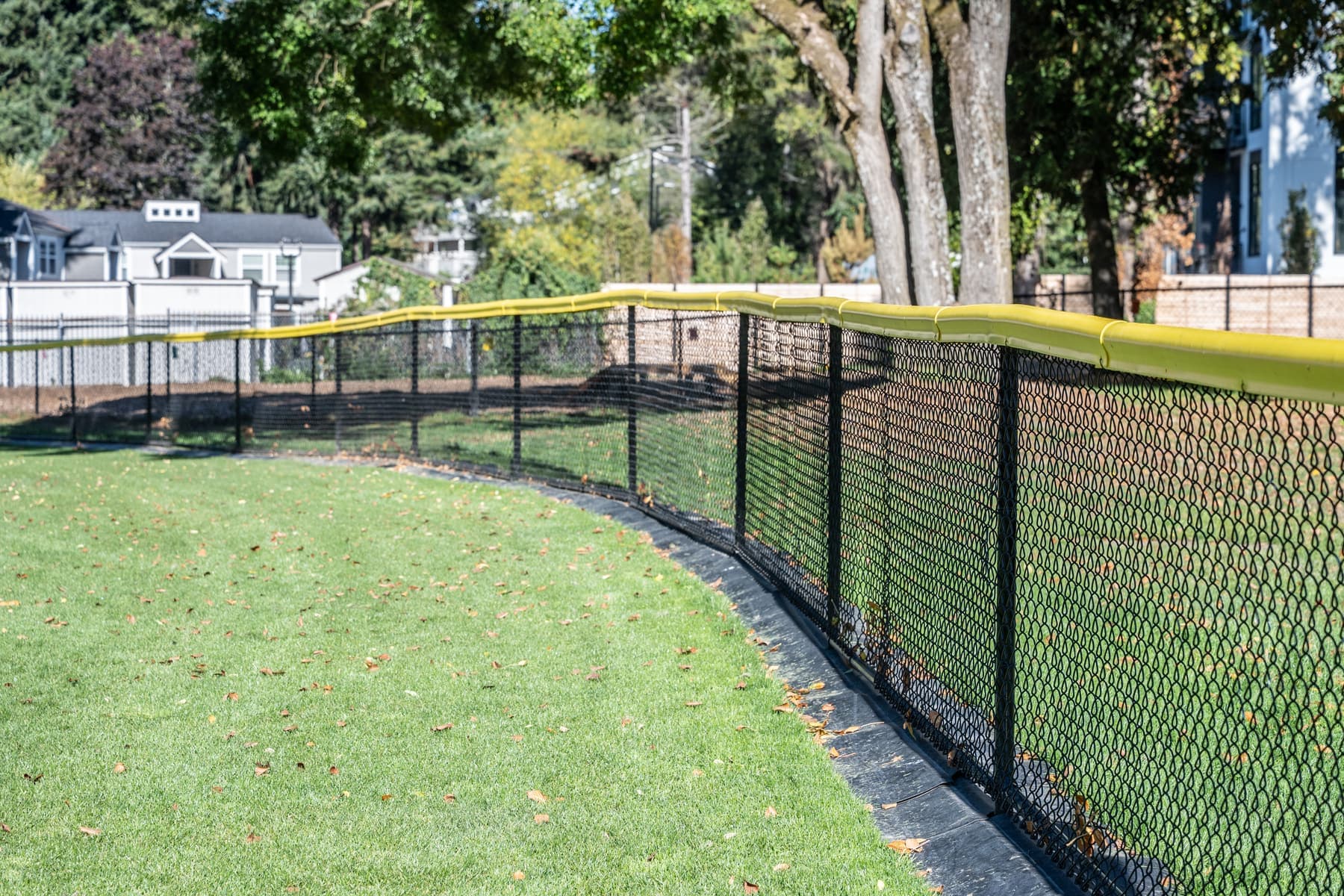 Black chain-link outfield fence with a yellow safety cap curving along a ballfield