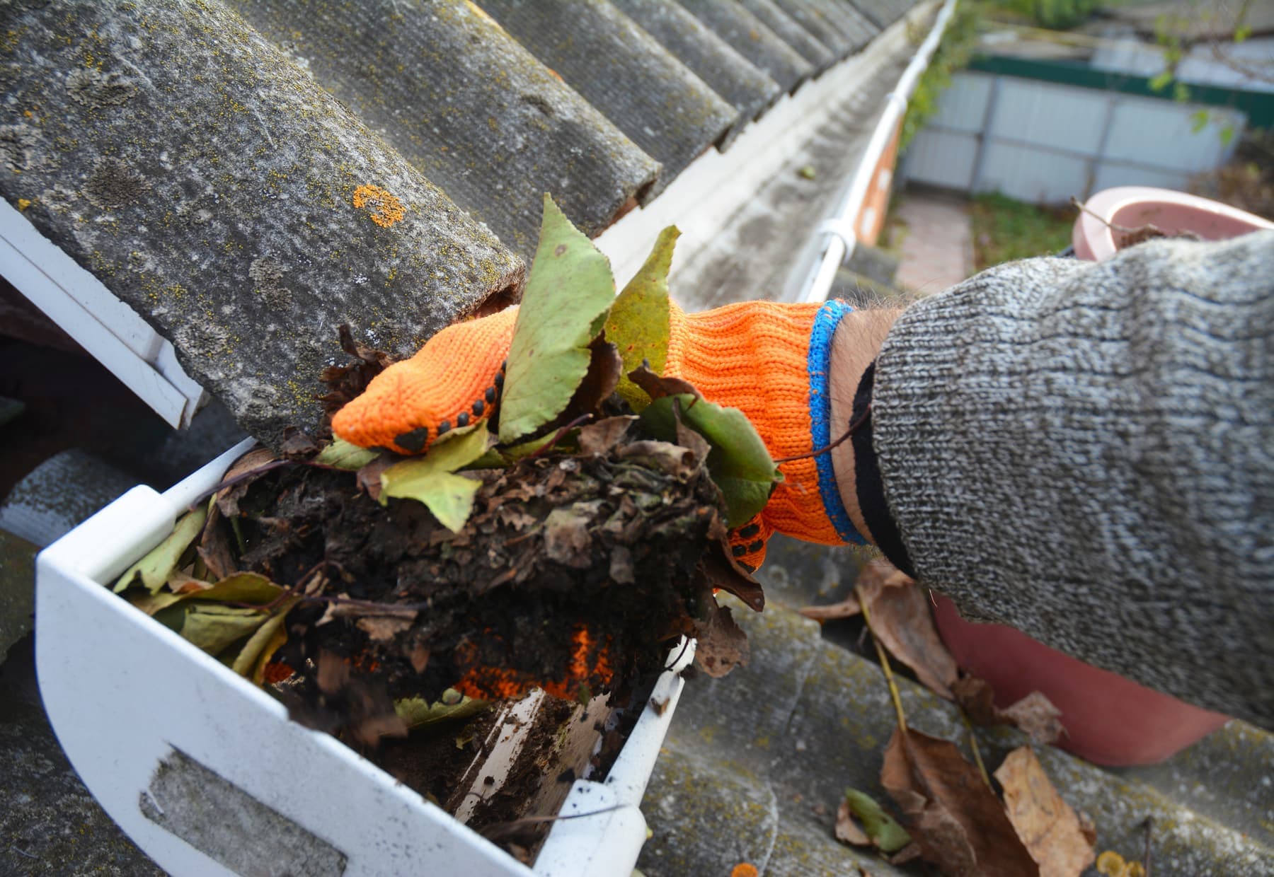 Gloved hand clearing leaves and debris from a gutter